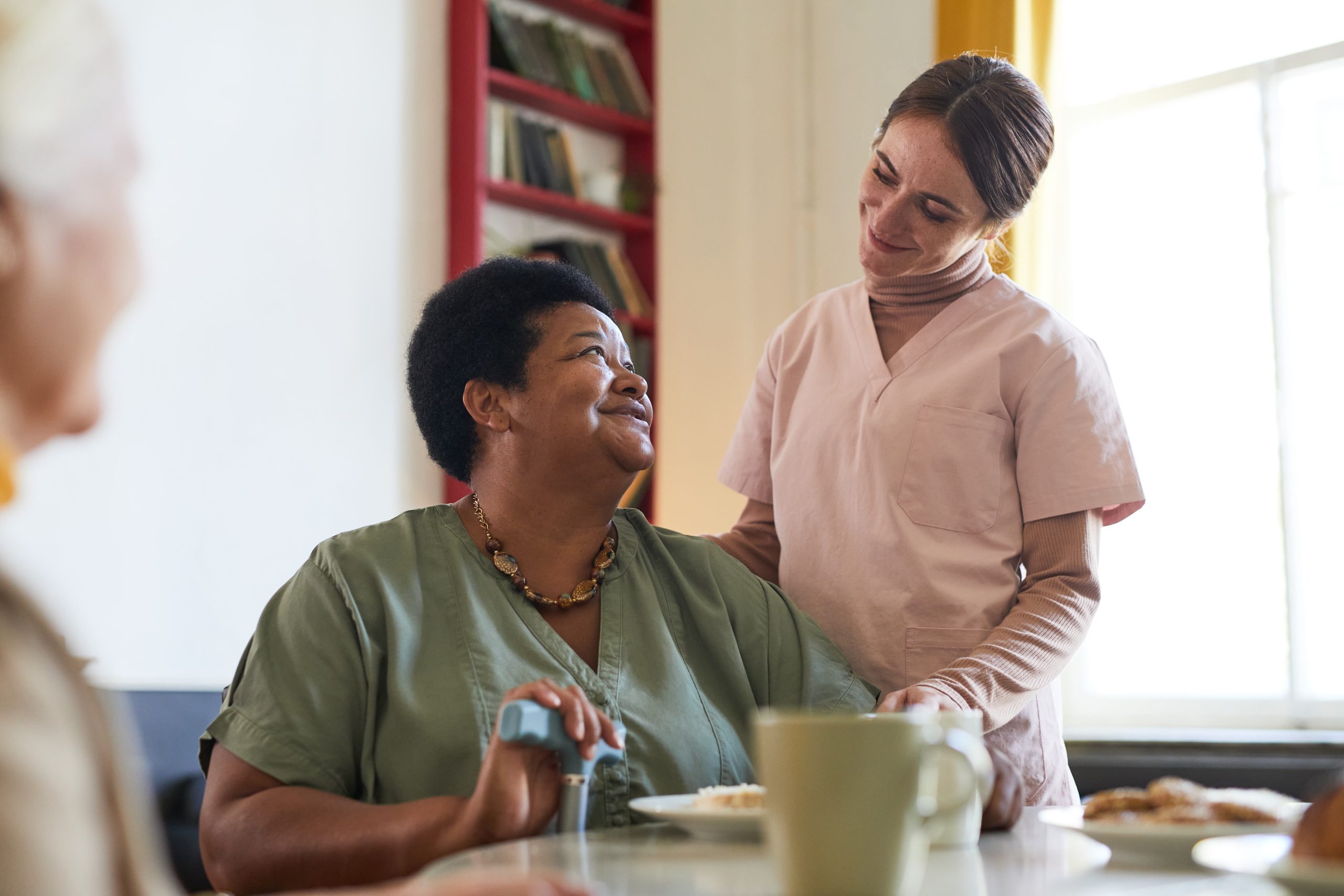 portrait-smiling-young-woman-assisting-female-patient-dinner-nursing-home-copy-space (1)